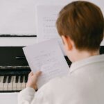 A child focused on reading sheet music at a piano, emphasizing musical learning.