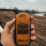 Hand holding a Terra-P dosimeter in an outdoor setting measuring radiation levels.