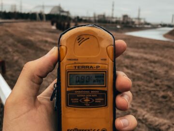 Hand holding a Terra-P dosimeter in an outdoor setting measuring radiation levels.