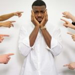 Worried man surrounded by pointing fingers, symbolizing bullying and social pressure.