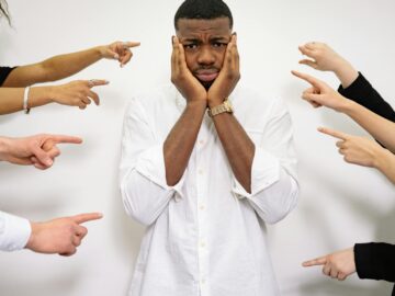 Worried man surrounded by pointing fingers, symbolizing bullying and social pressure.