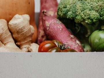 A variety of fresh organic vegetables including ginger, sweet potatoes, and broccoli in a cardboard box.