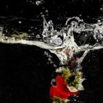 A vibrant strawberry plunges into clear water against a black background, creating an elegant splash effect.