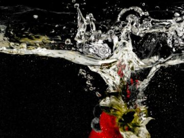 A vibrant strawberry plunges into clear water against a black background, creating an elegant splash effect.