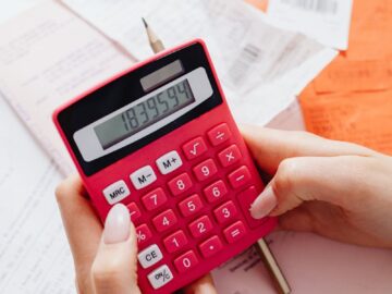 A person calculating finances on a red calculator surrounded by documents.