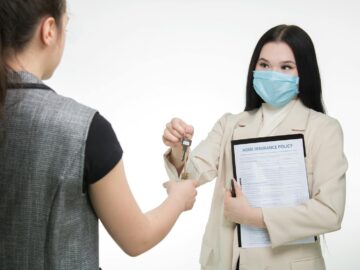 Real estate agent in a face mask hands keys to a client, illustrating safe business practices.
