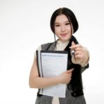Asian woman smiling while holding a home insurance policy and a key, symbolizing new home ownership.