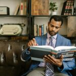 Focused businessman in a suit reading a financial planning book in office setting.