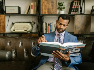 Focused businessman in a suit reading a financial planning book in office setting.