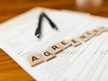 Scrabble tiles spelling 'AGREEMENT' on a lease document, emphasizing contractual themes.