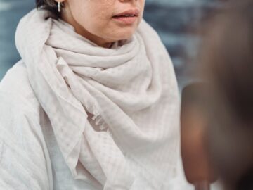 A woman in a light scarf participates in an interview indoors, captured during the day.
