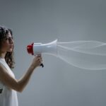 Woman using a megaphone emitting sound waves on a gray background.