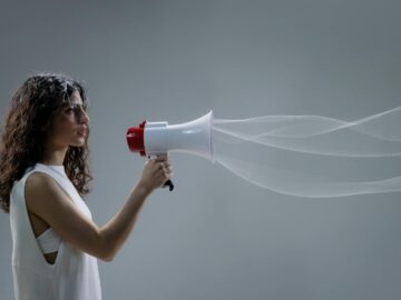 Woman using a megaphone emitting sound waves on a gray background.