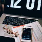 Laptop, smartphone, and financial document on a desk with clock display.