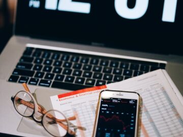 Laptop, smartphone, and financial document on a desk with clock display.