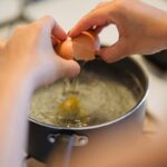 A person cracks an egg into a pot of boiling water, preparing a poached egg.