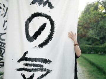 An individual holds a Japanese calligraphy banner in an outdoor garden setting.