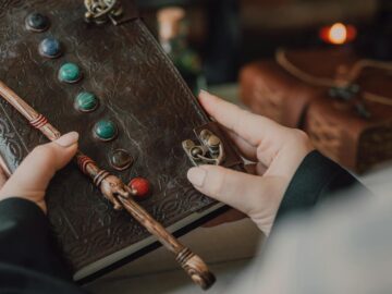 Hands holding a decorative journal and wand, evoking a magical and mystical theme.