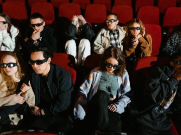 Group of people watching a movie in 3D glasses, expressing excitement and surprise.