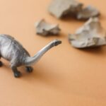 Close-up of a plastic dinosaur toy on a brown surface with paper rocks.