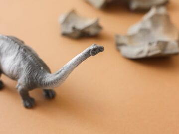 Close-up of a plastic dinosaur toy on a brown surface with paper rocks.
