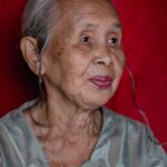 Portrait of an elderly woman with gray hair against a red background, exuding wisdom and serenity.