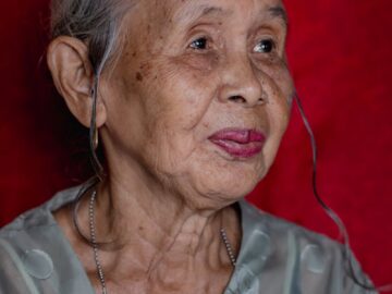 Portrait of an elderly woman with gray hair against a red background, exuding wisdom and serenity.