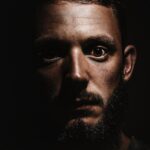 Close-up of a serious man with a beard in a dramatic shadowed portrait.