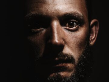 Close-up of a serious man with a beard in a dramatic shadowed portrait.