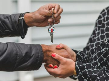 Close-up of a realtor handing over a house key to a new homeowner, symbolizing ownership and investment.