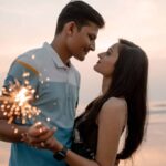 Loving couple holding sparklers at the beach during sunset, sharing a romantic moment.