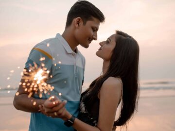 Loving couple holding sparklers at the beach during sunset, sharing a romantic moment.