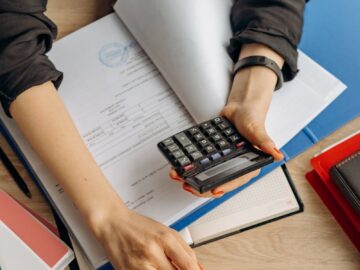A business professional uses a calculator among documents and laptop on a desk for financial tasks.