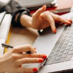 Close-up of hands with red nails typing on a laptop keyboard, depicting a productive work environment.