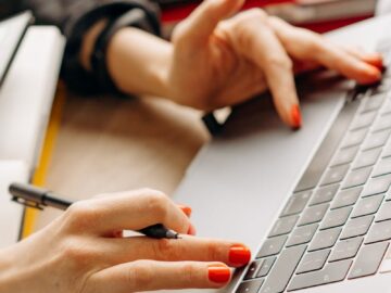 Close-up of hands with red nails typing on a laptop keyboard, depicting a productive work environment.