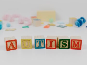 Colorful blocks spelling 'autism' with blurred toys in background.