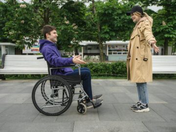 A joyful couple in a park, featuring a man in a wheelchair and a woman in a coat, sharing a moment.