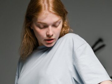 A startled young woman looks at a cockroach on her shirt indoors, conveying fear.