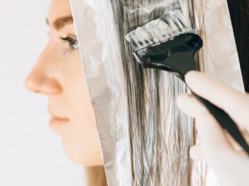 Close-up of a woman getting hair highlights with foil and dye brush.
