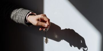 Hand with a key casting a dramatic shadow on a wall, symbolizing property or ownership.