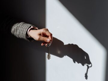 Hand with a key casting a dramatic shadow on a wall, symbolizing property or ownership.