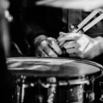 Artistic black-and-white photo showing a drummer's hands on a snare drum in a close-up view.