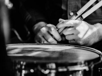 Artistic black-and-white photo showing a drummer's hands on a snare drum in a close-up view.
