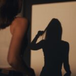 A woman indoors with her silhouette casting a dramatic shadow on the wall.