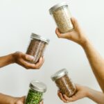 Four hands holding glass jars of grains and legumes, emphasizing kitchen organization.