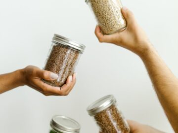Four hands holding glass jars of grains and legumes, emphasizing kitchen organization.