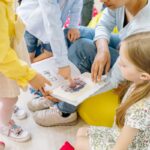 Preschool children gathered around a teacher reading a storybook indoors.