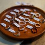 A collection of assorted handmade jewelry rings displayed on a wooden plate with labeled tags.