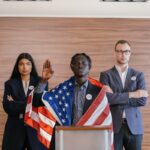 Three diverse political candidates taking an oath with an American flag at a podium indoors.