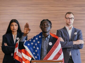 Three diverse political candidates taking an oath with an American flag at a podium indoors.